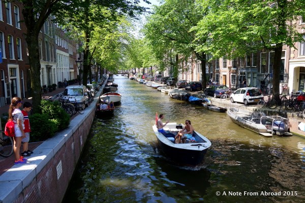Children watch as small boats slowly cruise by. Many of the canals are tree lined.