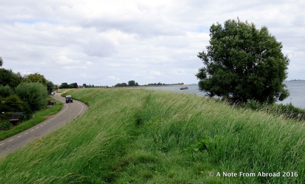 Earthen dike covered with grass with the water level higher than the road